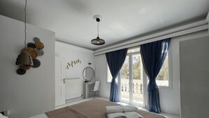 Een slaapkamer met een bed, nachtkastje, spiegel en raam met gordijnen.