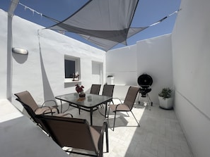 Une terrasse avec une table et des chaises, un barbecue et des plantes en pot.