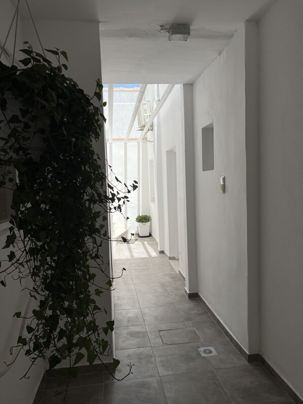 A narrow hallway with white walls, a tiled floor, and a hanging plant on the left. - 3 Bedroom House included car rental-Heated Jacuzzi (santorini)