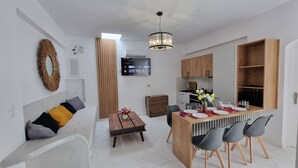 Een moderne woonkamer met een bank, een eettafel voor vier personen, en een keuken met houten kastjes en een inbouwoven.