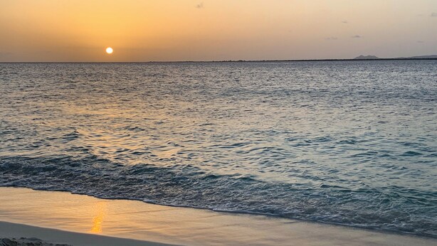 Una playa con aguas tranquilas que reflejan la puesta de sol.