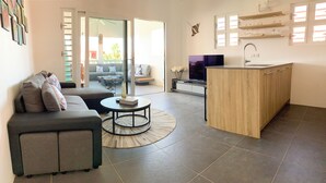 Una sala de estar moderna con un sofá gris, una mesita redonda y una zona de cocina con mostrador de madera y un lavamanos.