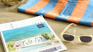 Un magazine, un sac à rayures, une paire de lunettes de soleil et un bol décoratif posés sur une table en bois.