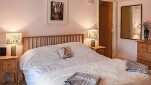A bedroom with a large bed, two bedside tables with lamps, a wooden headboard, a framed picture on the wall, a mirror, and a dresser with a vase of flowers. - 2 bedroom accommodation in Middlesmoor, near Pateley Bridge (Middlesmoor, near Pateley Bridge)