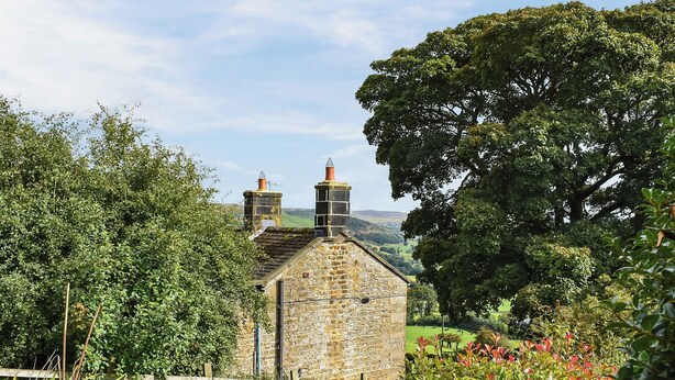 A stone building with two chimneys, surrounded by lush greenery and a wooden fence. - 2 bedroom accommodation in Middlesmoor, near Pateley Bridge (Middlesmoor, near Pateley Bridge)