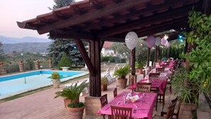 Un patio exterior con mesas y sillas, piscina y plantas en macetas.