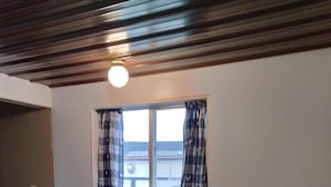 A dining area with a wooden table and four chairs, a window with curtains, and a ceiling with a light fixture.