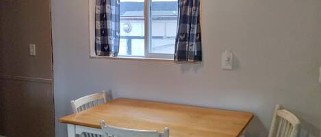 A dining area with a wooden table and four chairs, a window with curtains, and a ceiling with a light fixture.
