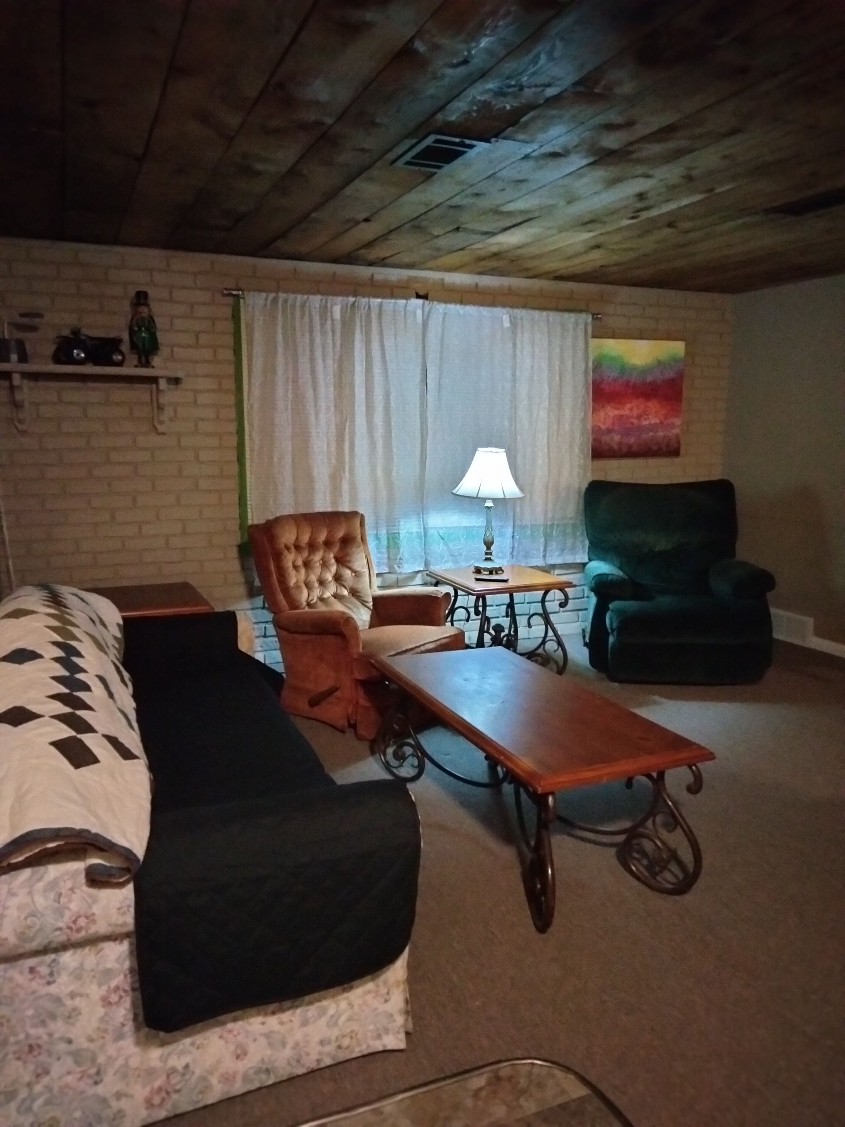 Una habitación acogedora con una cama, un sillón capitonado, un sillón verde, una mesita y una lámpara.