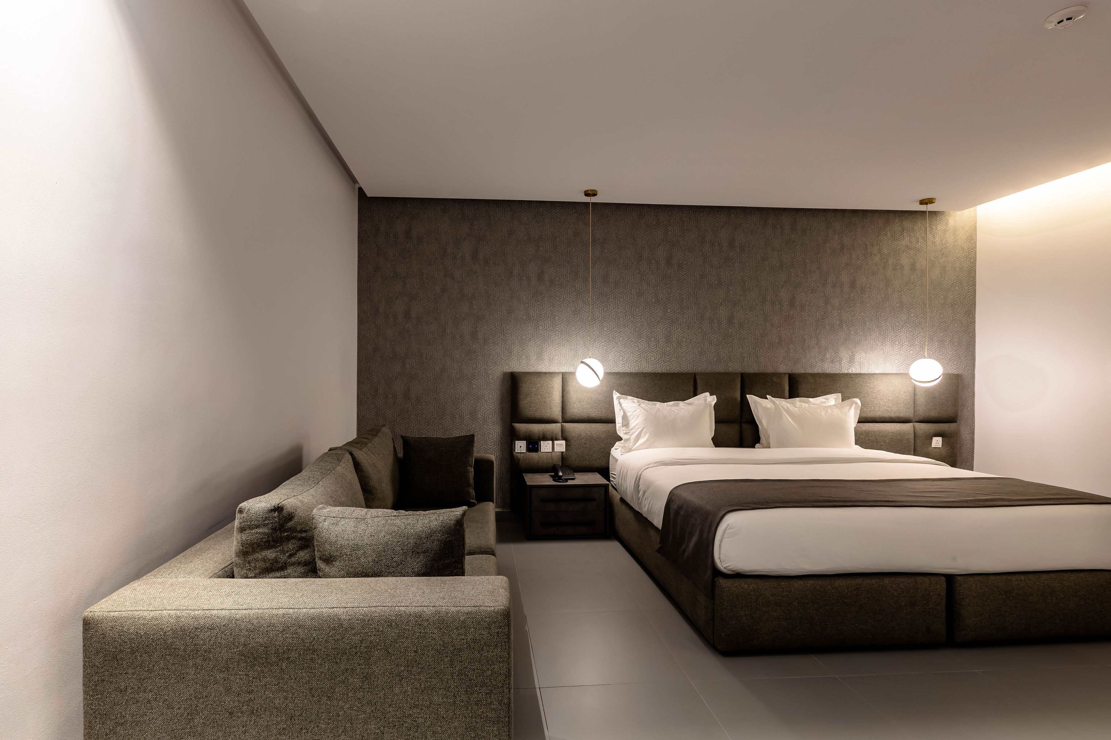 A modern bedroom with a large bed, a nightstand, a sofa, and a wall-mounted light fixture.