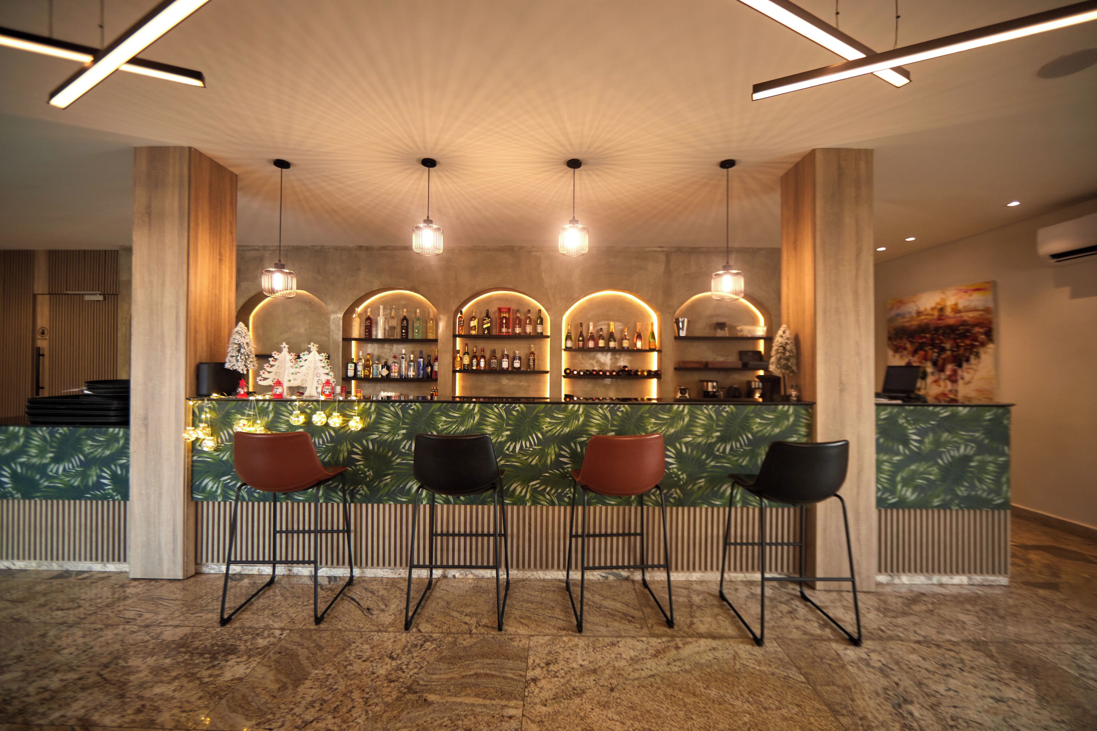 A bar area with a counter, three stools, and shelves of bottles.