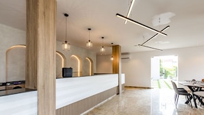 A modern reception area with a wooden reception desk, pendant lighting, and a view of the outdoor garden. - The Panama  (Abuja)