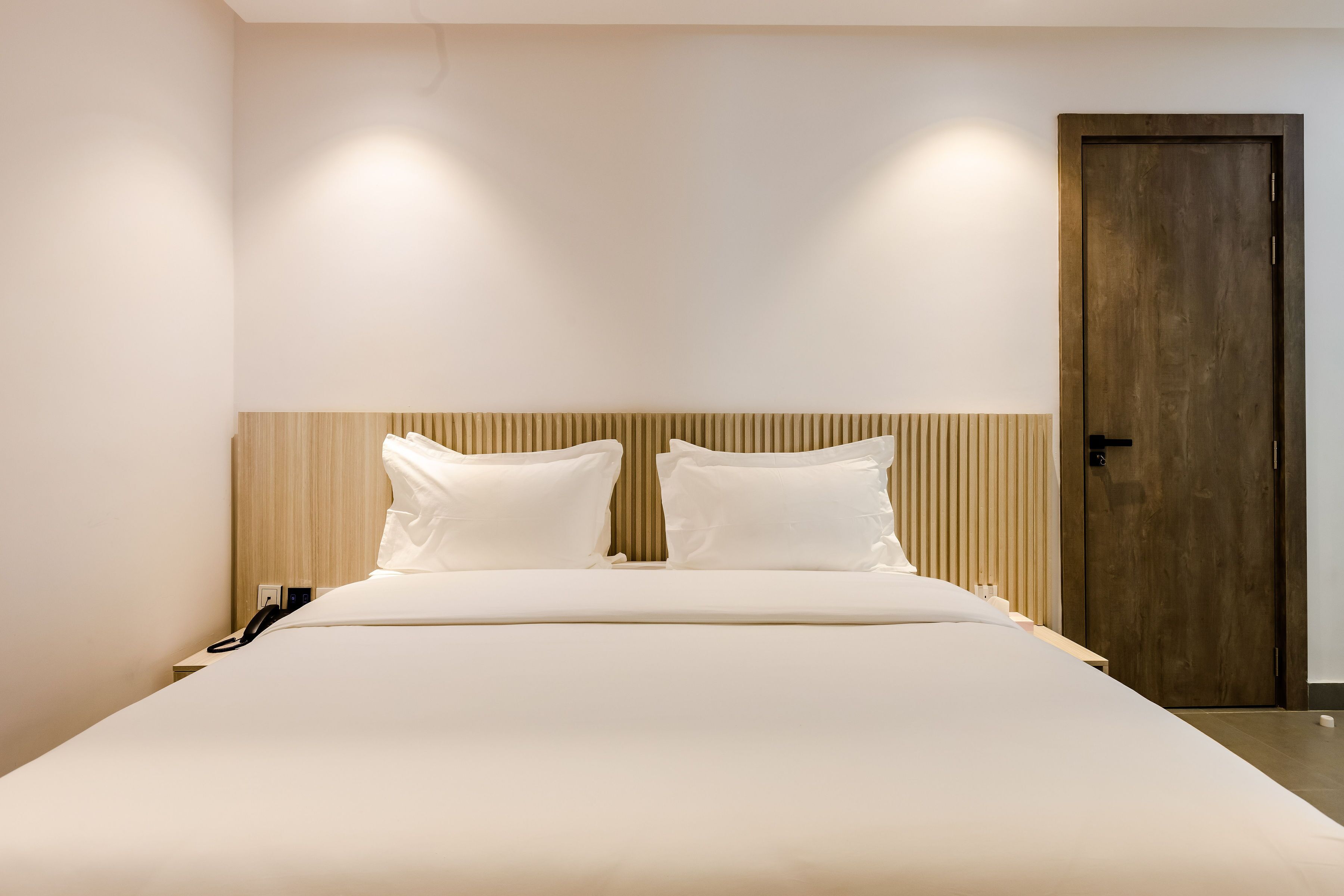 Een net opgemaakt bed met een houten hoofdbord, een bedtelefoon en een houten deur in een moderne kamer.
