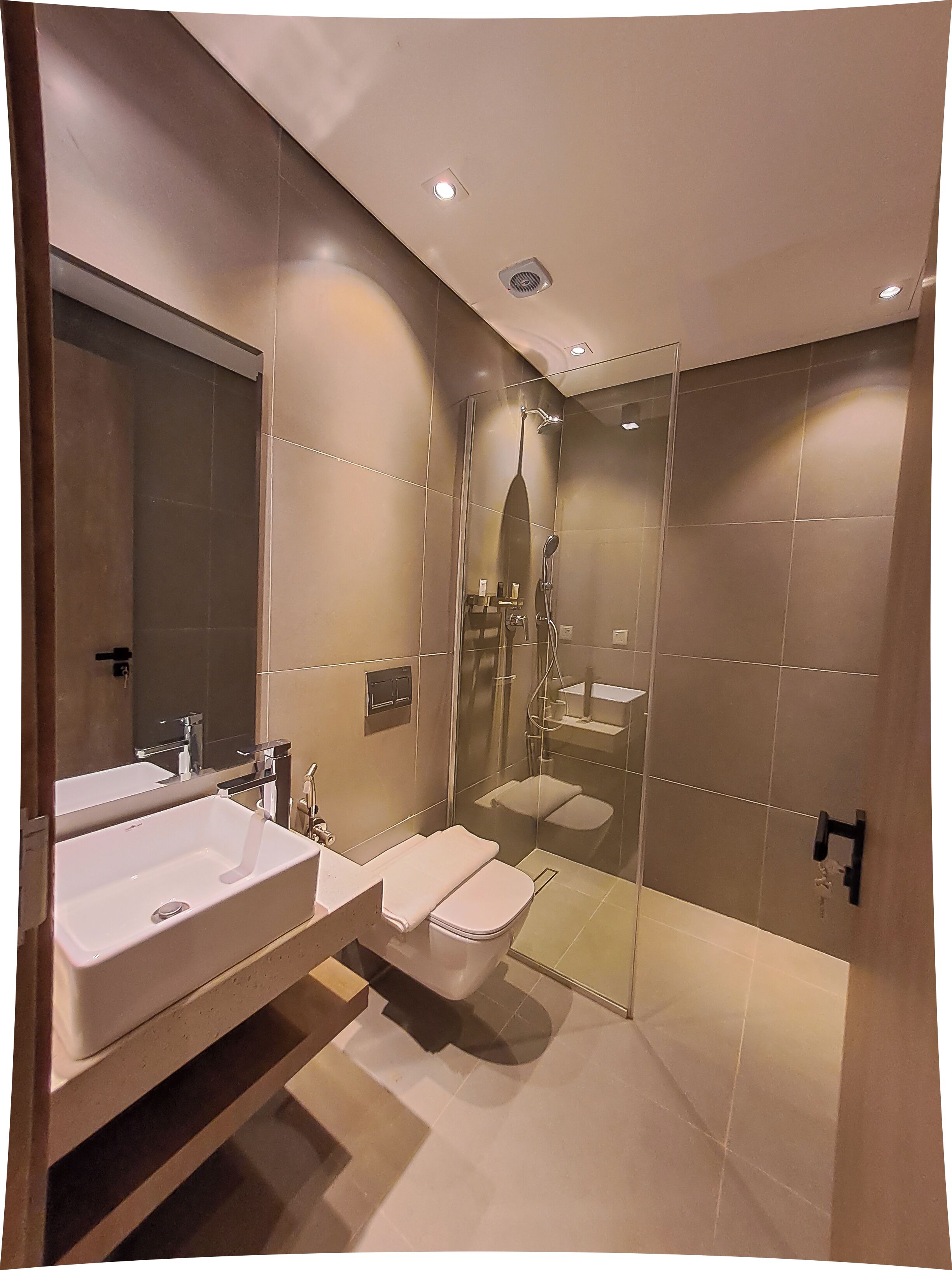 A modern bathroom with a large mirror, two sinks, a toilet, and a shower area.