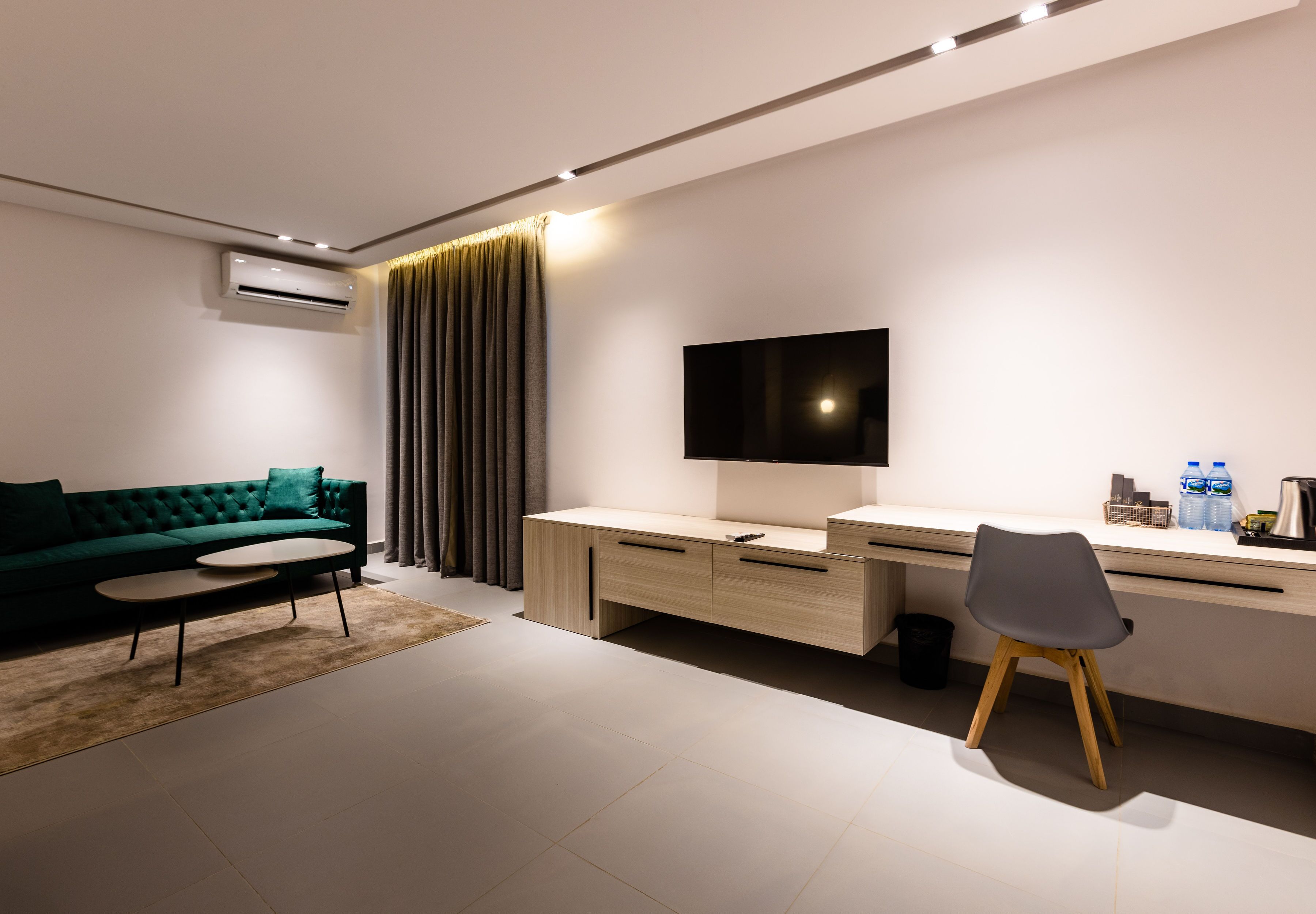 Una sala de estar moderna con un sofá verde, una mesita de centro, un escritorio con una silla y un televisor de pantalla plana montado en la pared.