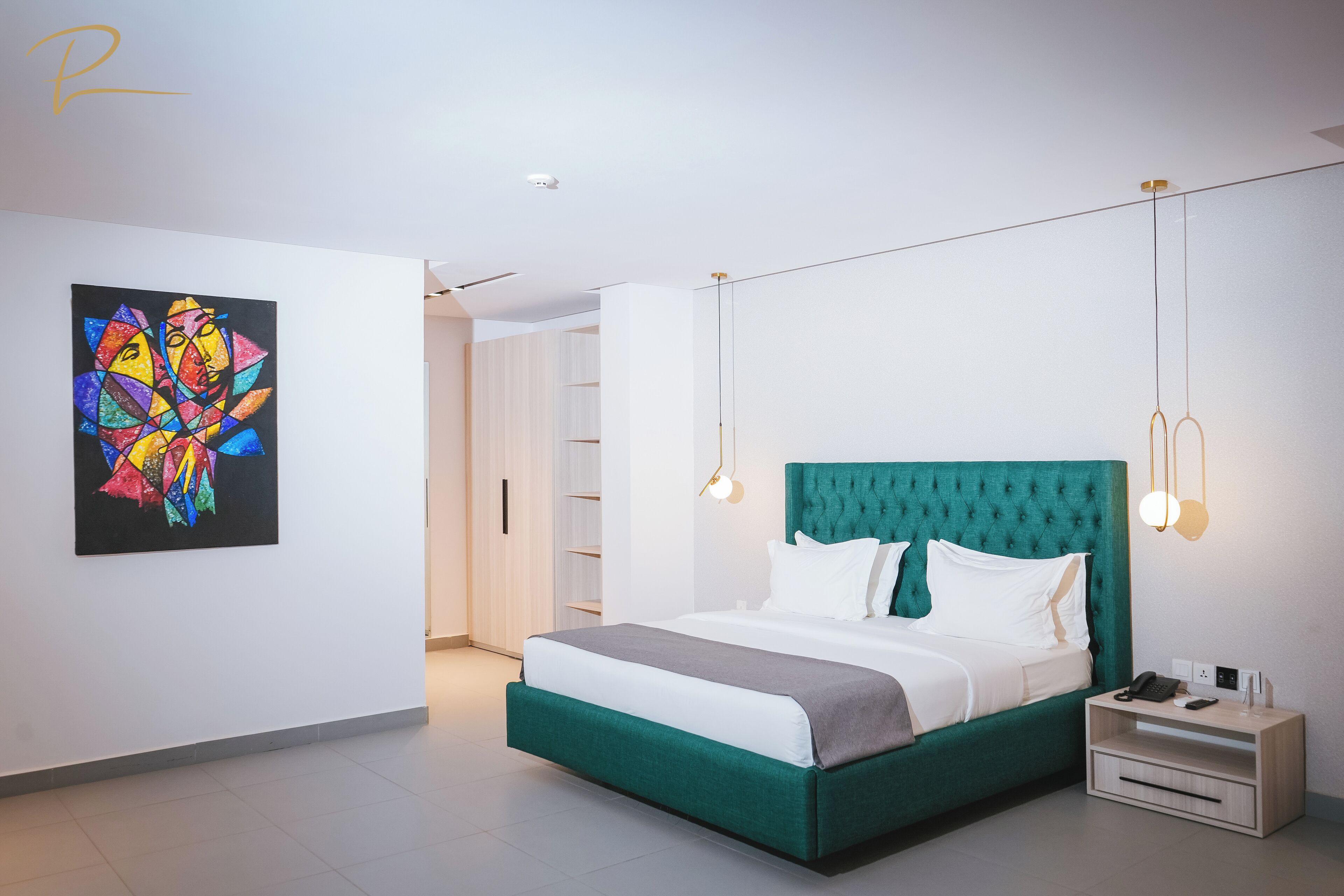 A modern bedroom with a teal bed, white bedding, and a colorful abstract painting on the wall.