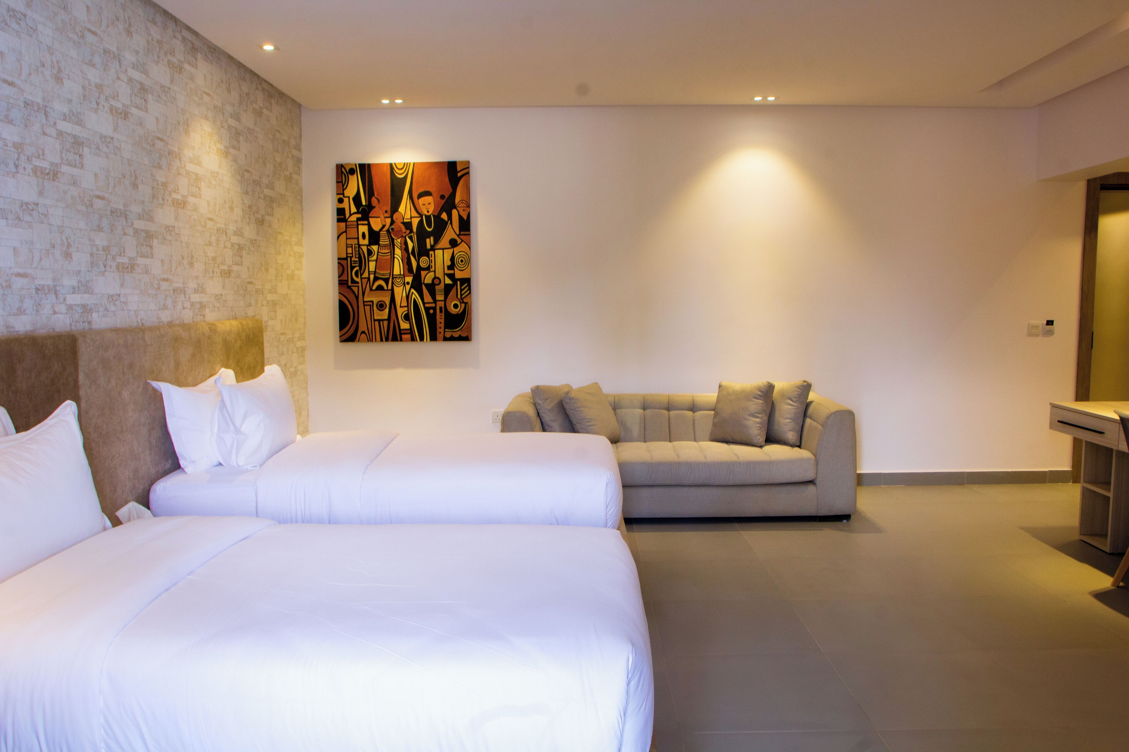 A hotel room with two beds, a sofa, and a painting on the wall.