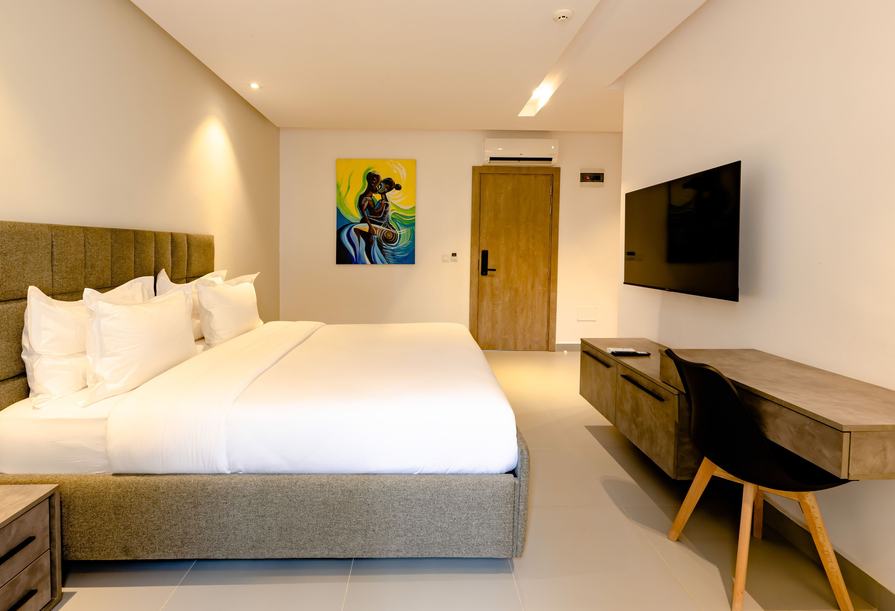 A modern hotel room with a large bed, a desk with a chair, a flat-screen TV, and a painting on the wall.