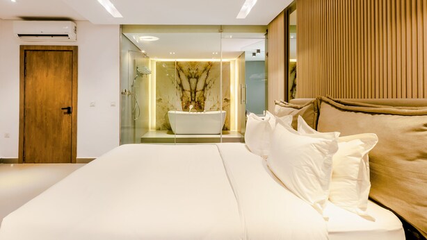 A modern hotel room with a large bed, a built-in bathtub, and a wooden door. - The Panama  (Abuja)