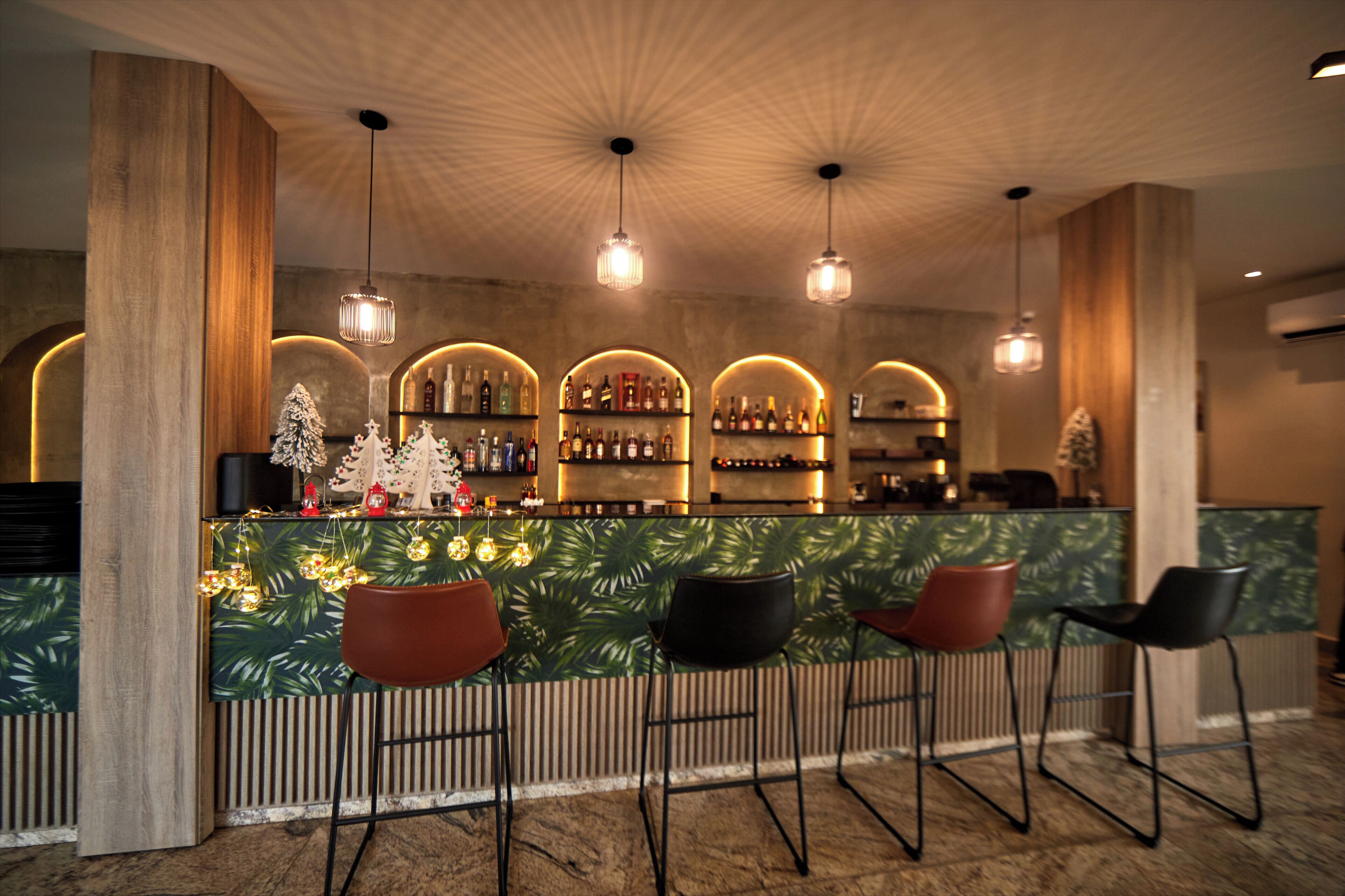 A bar area with a wooden counter, three bar stools, and a tropical leaf-patterned wall.