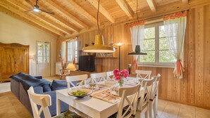 A cozy room with a wooden ceiling, a dining table set with plates and flowers, a sofa, and a television. - Lovely home in Farnese (Farnese)