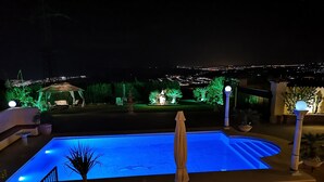A swimming pool with lounge chairs and an umbrella, surrounded by well-lit garden areas and a view of the city at night. - Villa Roca, Lejlighed til 2 Personer, 3km til Estepona (AN)