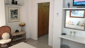 A bedroom with a bed, a chair, a small table with a vase, a television, and a wardrobe. - Villa Roca, Lejlighed til 2 Personer, 3km til Estepona (AN)