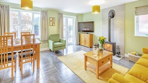 A living room with a dining area, a television, a fireplace, and large windows. - 3 bedroom accommodation in Upper Soudley (Upper Soudley)