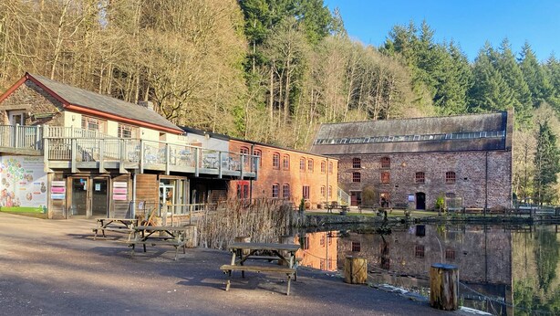 A historic building with a balcony, a wooden bench, and a pond in the foreground. - 3 bedroom accommodation in Upper Soudley (Upper Soudley)