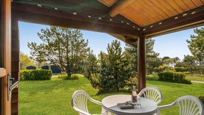 Une terrasse couverte avec une table ronde et quatre chaises, donnant sur une pelouse bien entretenue et des arbres.