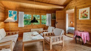 L’intérieur d’un chalet accueillant, avec des murs en bois, une table à manger, deux chaises, un canapé, une lampe et une fenêtre avec des rideaux.