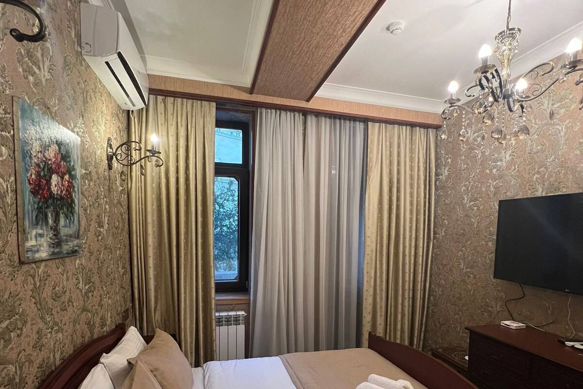 A hotel room with a large bed, a television, a chandelier, and a window with curtains.
