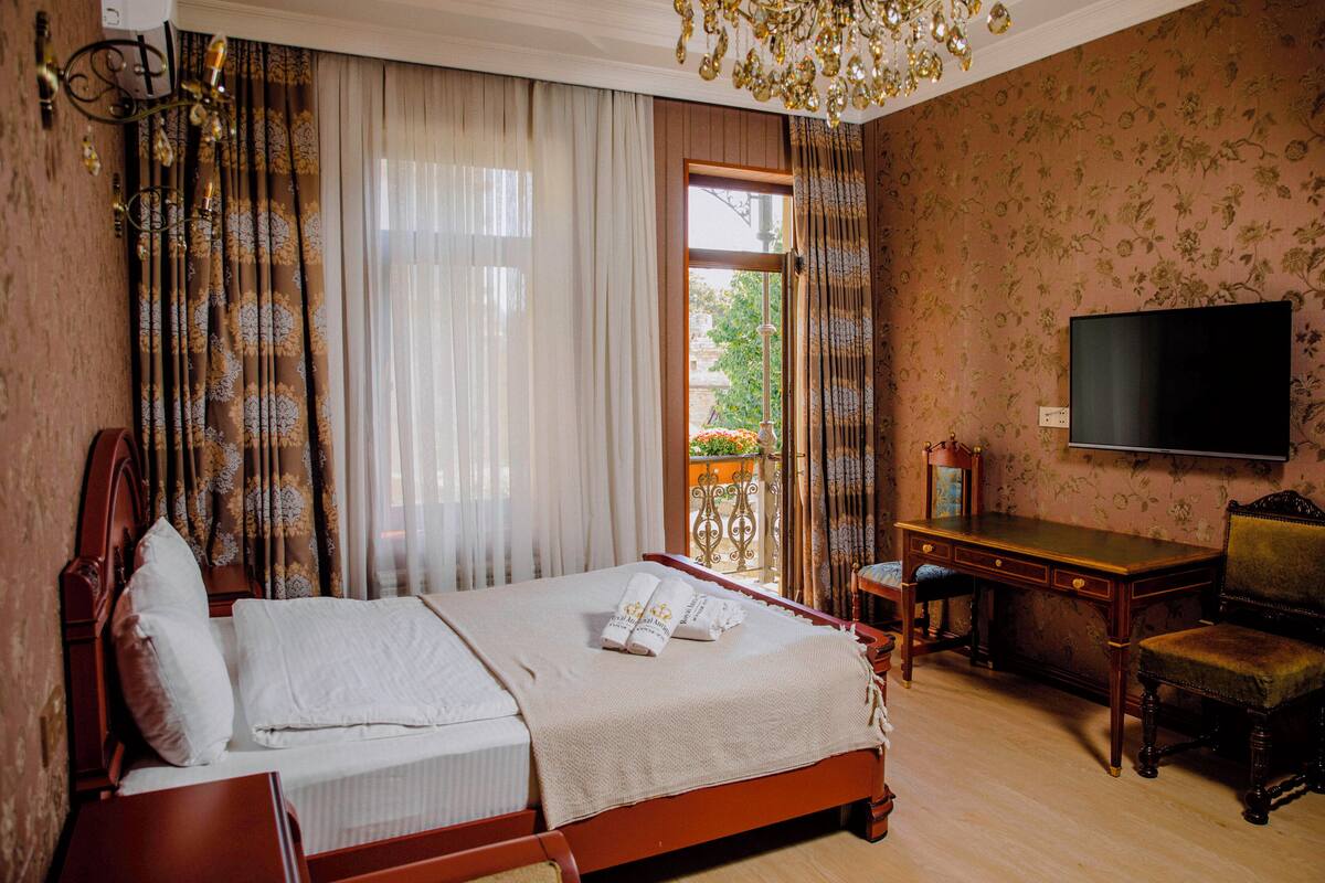 A hotel room with a bed, a desk, a chair, a television, and a balcony with a view of greenery.