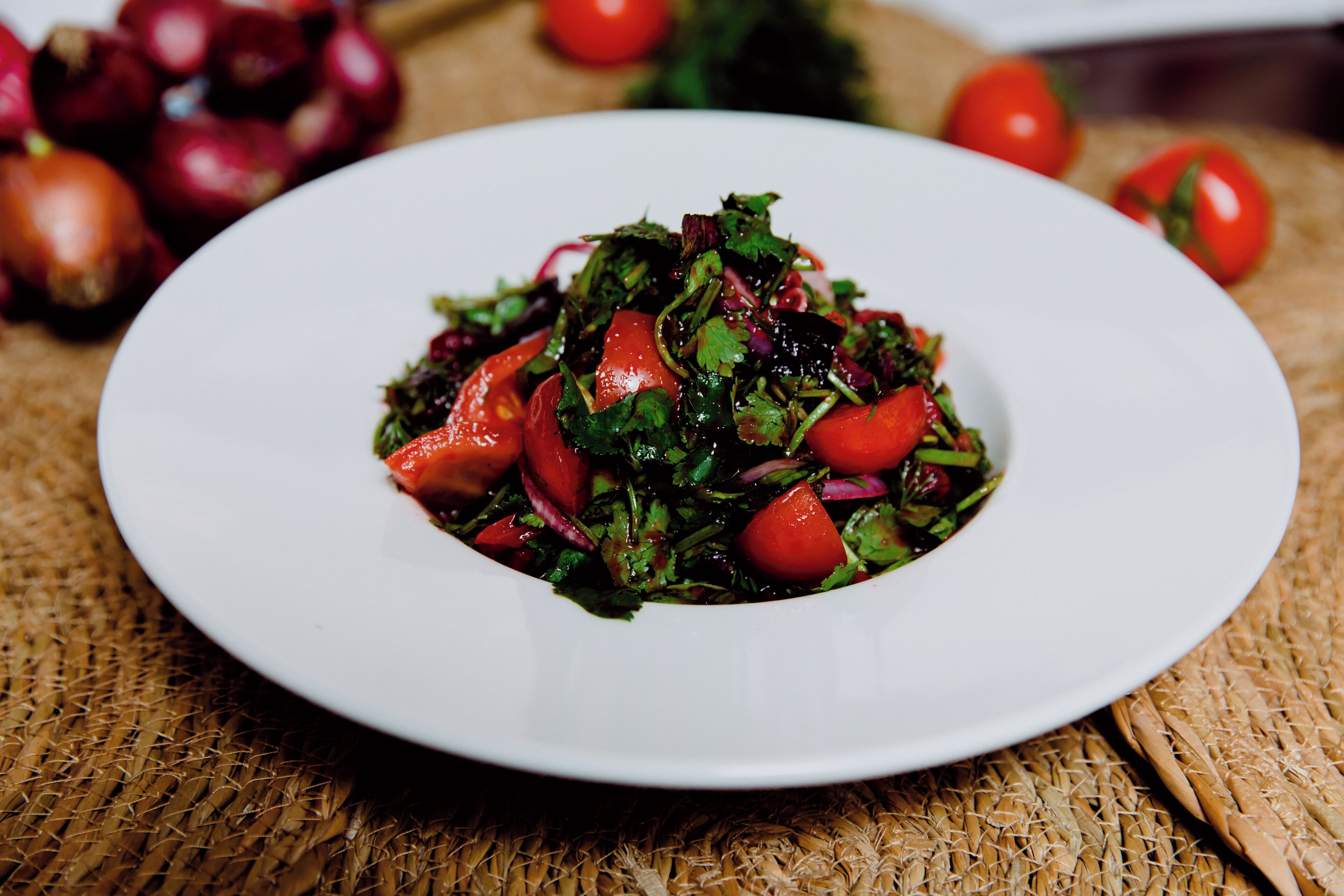 Een witte schaal met een salade op een geweven mat.