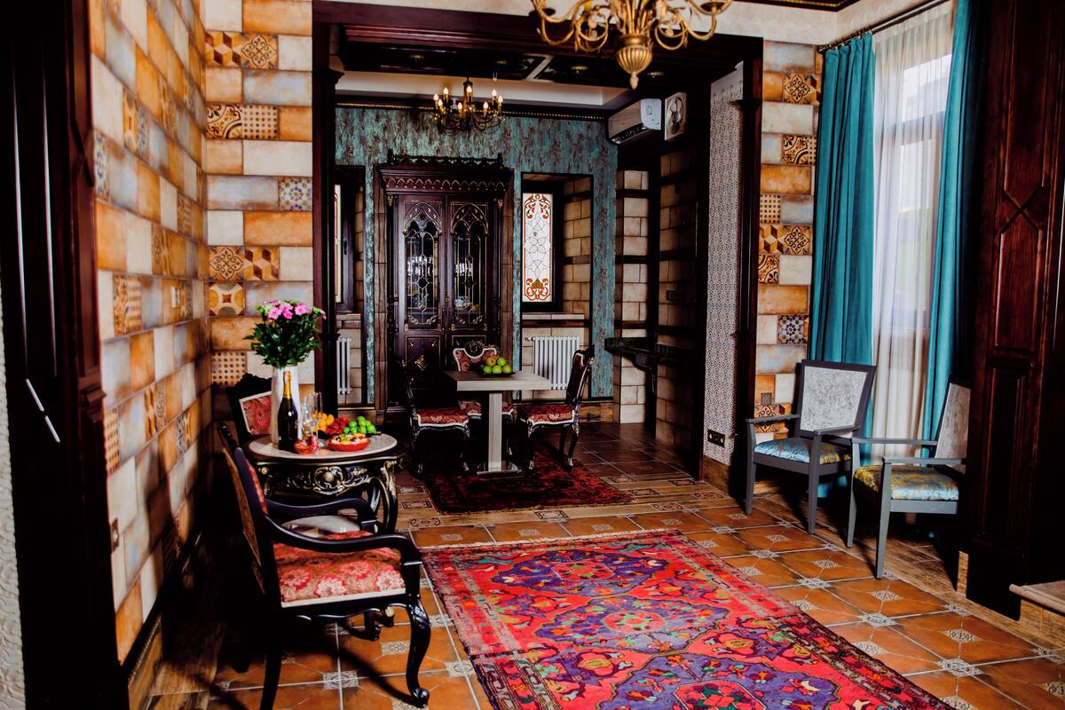 A traditional interior with patterned walls, a dining area with a table and chairs, and a large decorative rug.