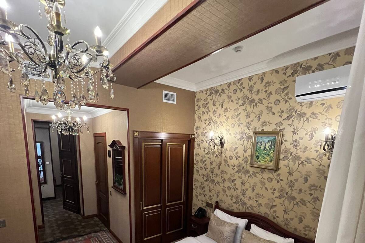 A bedroom with a large bed, a chandelier, a wardrobe, and a floral wallpaper.