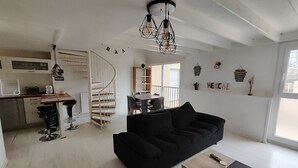 Un espacio habitable moderno con un sofá negro, una mesa de centro de madera y una escalera espiral que lleva a un balcón.