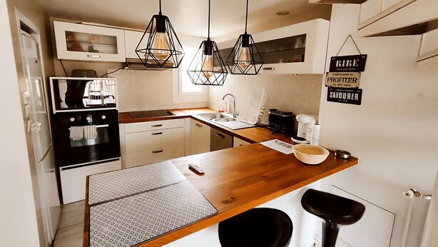 Una cocina moderna con encimera de madera, dos lámparas colgantes, horno empotrado, cafetera y un letrero en la pared.