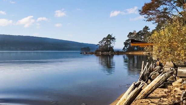 Un lac paisible, avec une jetée en bois qui s’avance sur l’eau, entouré d’arbres et dominé par une colline lointaine.