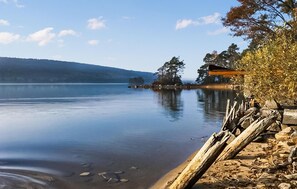 Un lago tranquilo con un muelle de madera que se adentra en el agua, rodeado de árboles y una colina distante.