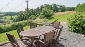 An outdoor seating area with a round wooden table and chairs, surrounded by gravel and greenery.