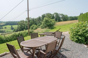 Ein Außenbereich mit Sitzgelegenheit, einem runden Holztisch und Stühlen, umgeben von Kies und Pflanzen.