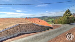 A stone building with a red-tiled roof, a paved road, and a green landscape in the background.