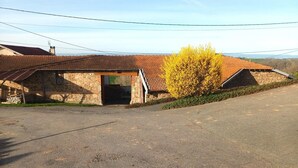 A stone building with a tiled roof, a covered entrance, and a parking area. - Majoa - Villecheneve (VILLECHENEVE)