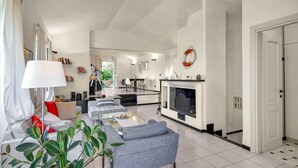 A modern living room with a sofa, a dining table, and a fireplace. There is a kitchen area in the background with a dining table and chairs. - 3 bedroom gorgeous home in Rapallo (Rapallo)