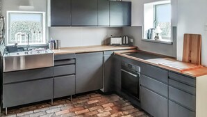 Cozinha compacta com armários escuros, bancada de madeira e piso de tijolos.