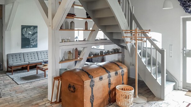 Quarto estilo loft com vigas de madeira aparentes, beliche, sofá cinza e um baú grande com detalhes em metal.