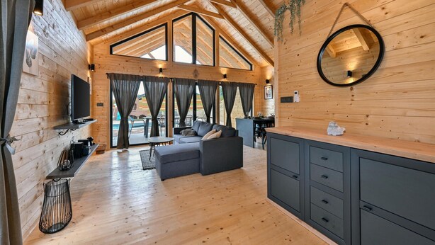 Ein gemütliches Cabin-Interieur mit Holzbalkendecke, einer Couch, einem Fernseher und einer Küchenzeile.