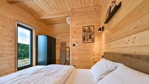 Ein Schlafzimmer einer Holzhütte mit Bett, Schrank und Fenster mit Blick ins Freie.