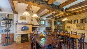 Un comedor rústico con una gran mesa de madera, varias sillas, una chimenea de piedra y vigas de madera a la vista.